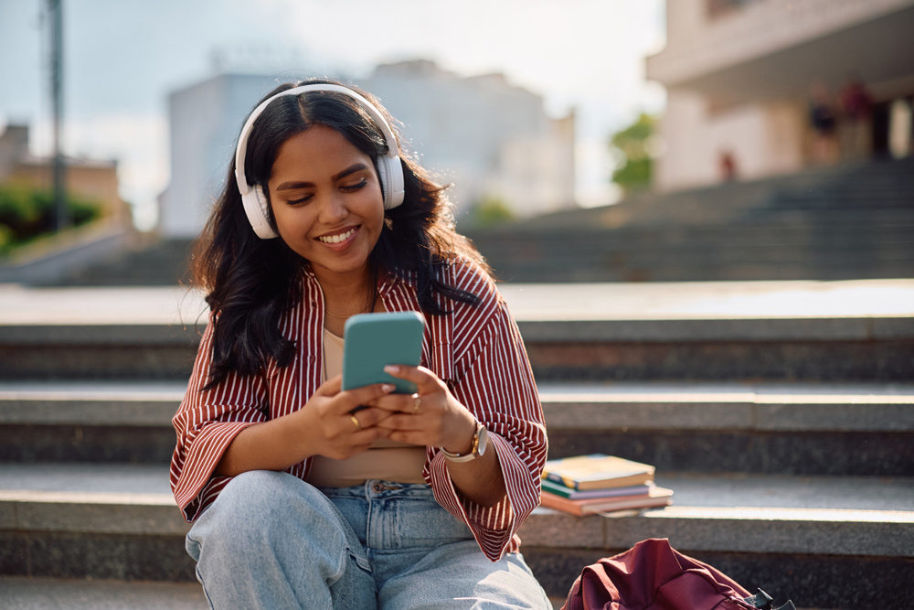 Happy female Indian student using smart phone after a lecture at university campus. Copy space