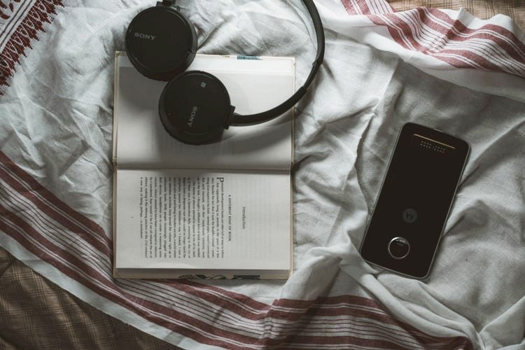 headphones on bed with phone and book