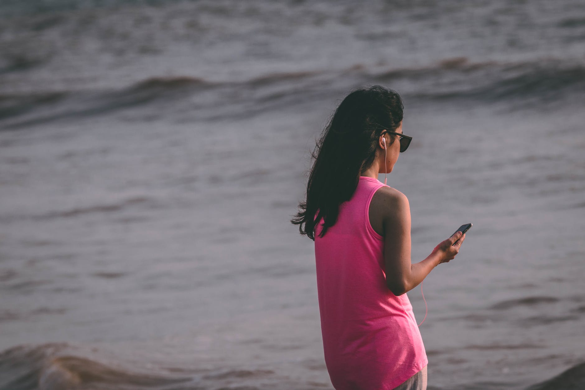 woman holding a phone on the shore while wearing earphones