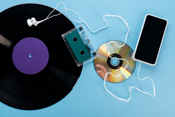 top view of vintage vinyl record, compact disk, earphones, audio tape and smartphone with blank screen on blue, evolution concept